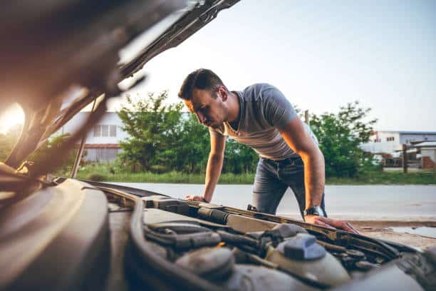 Jeune homme qui regarde sous le capot de sa voiture pour la réparer