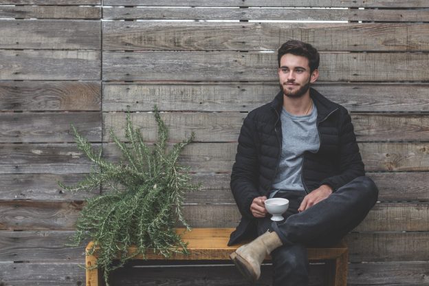 jeune homme assis sur un banc à côé d'une plante tenant une tasse